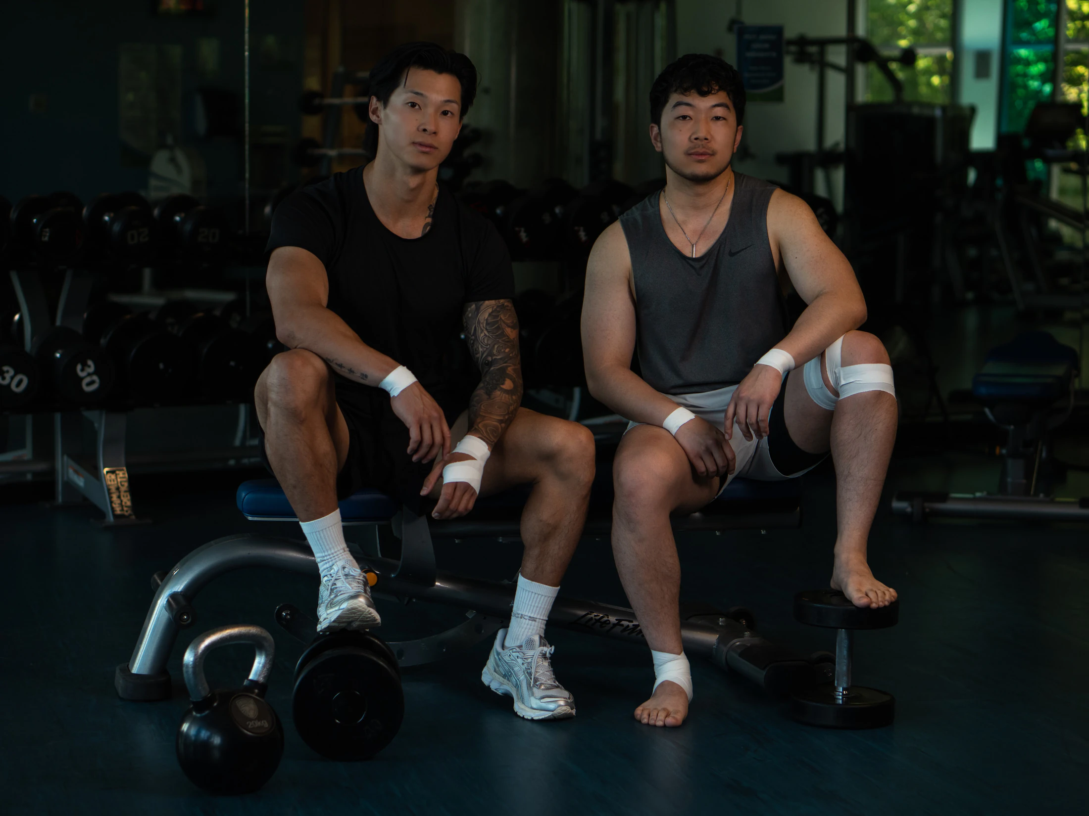 Two athletes with taped wrists and knees sitting on a gym bench
